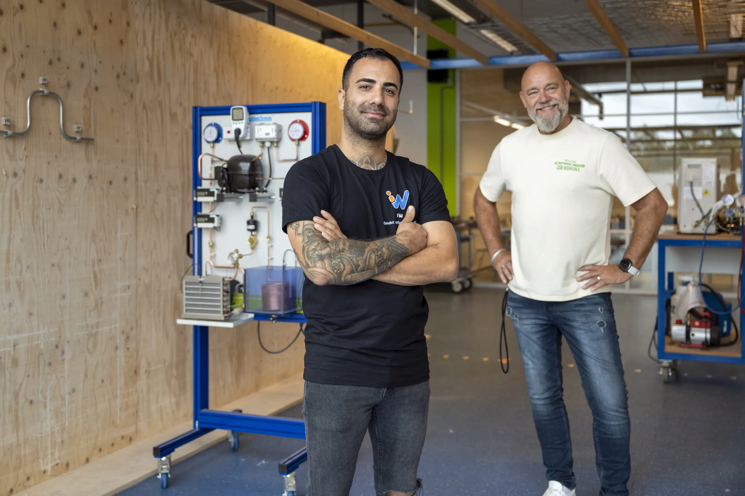 Docenten in een praktijkruimte voor techniekonderwijs, met gereedschap en opstellingen achter hen.