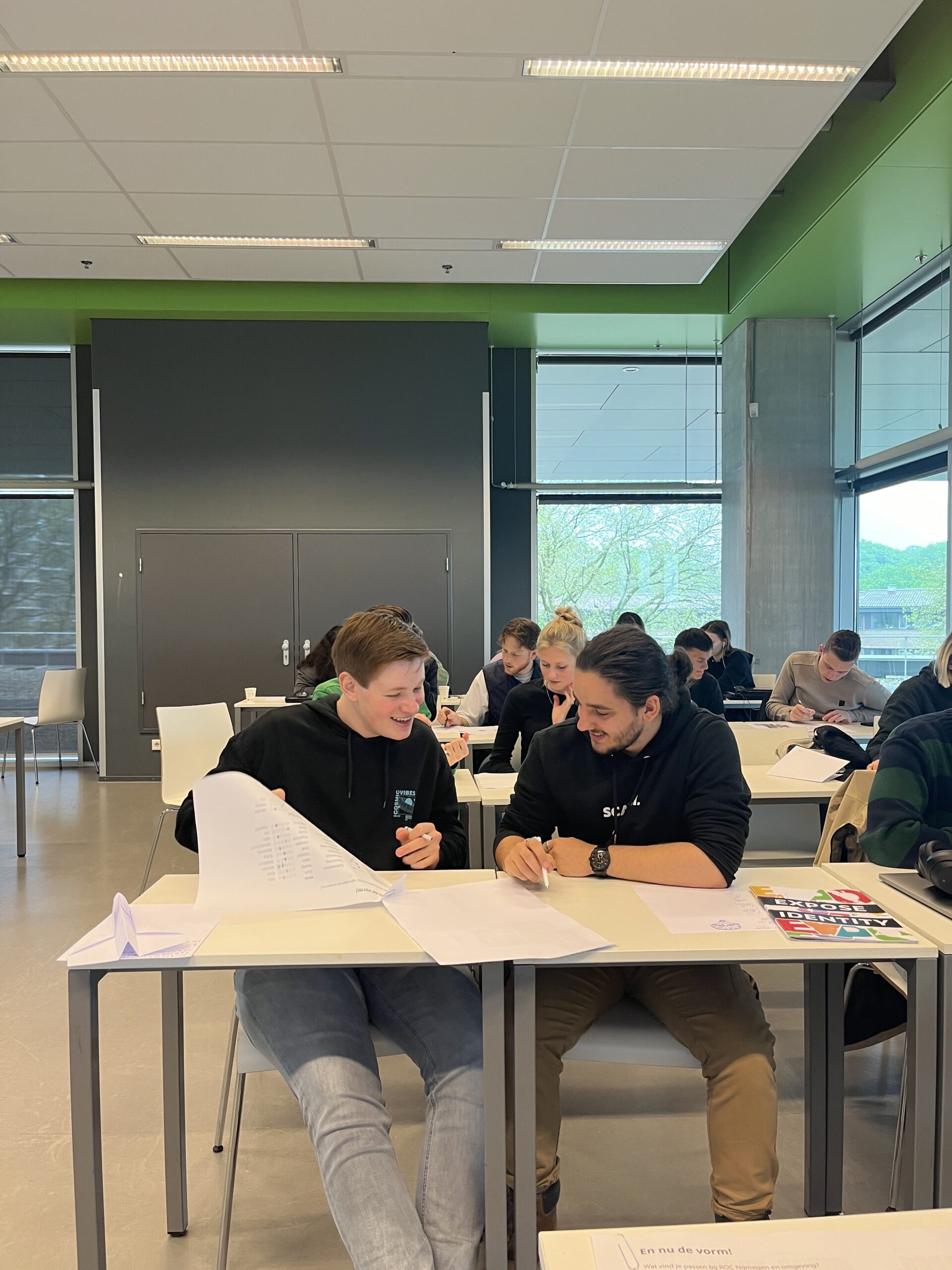 Twee studenten overleggen lachend aan tafel tijdens de co-creatie sessie.