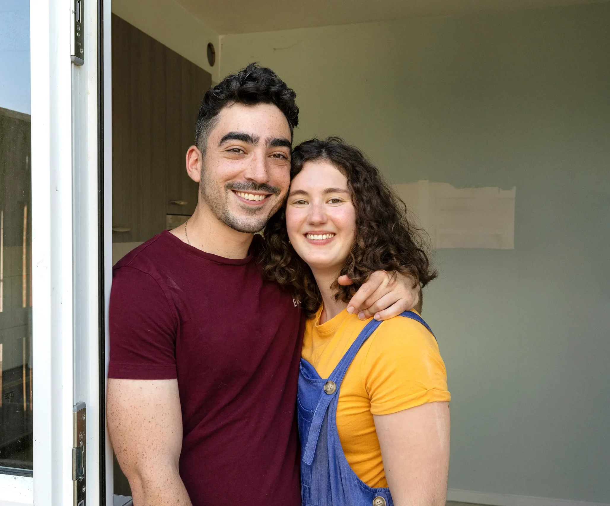 Jong stel staat lachend in de deuropening van hun nieuwe woning.