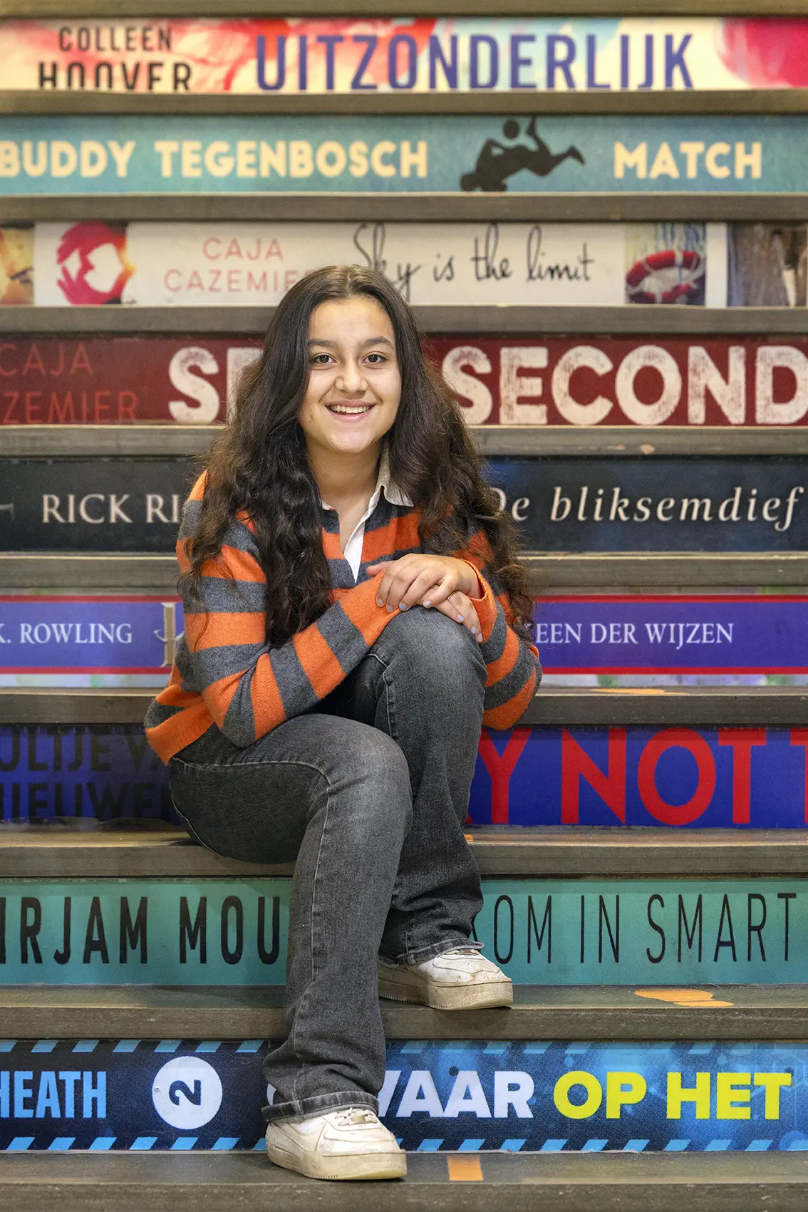 Lachende leerling zit op een trap met treden vol boekentitels.