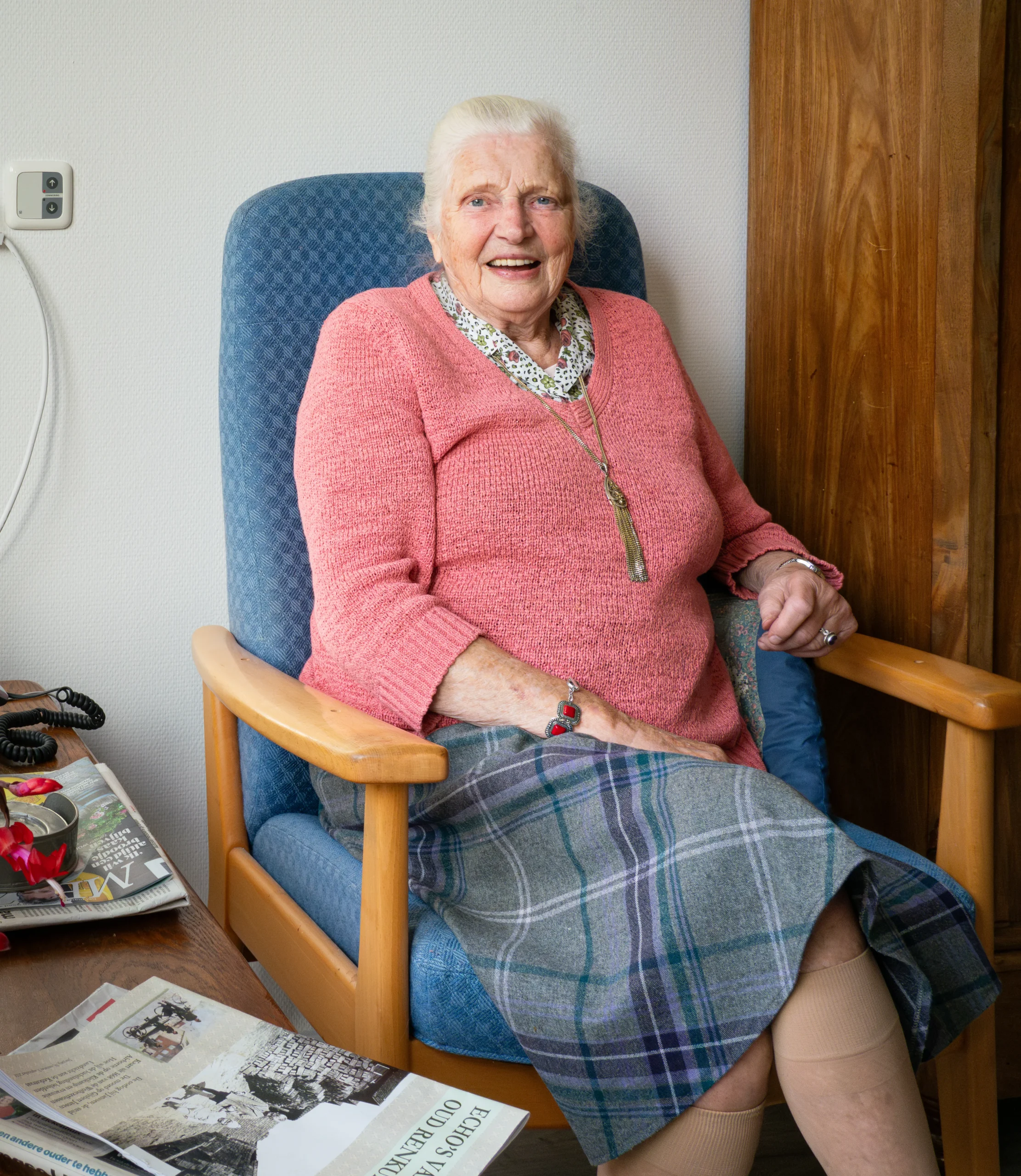 Oudere vrouw met roze trui zit in een comfortabele stoel.